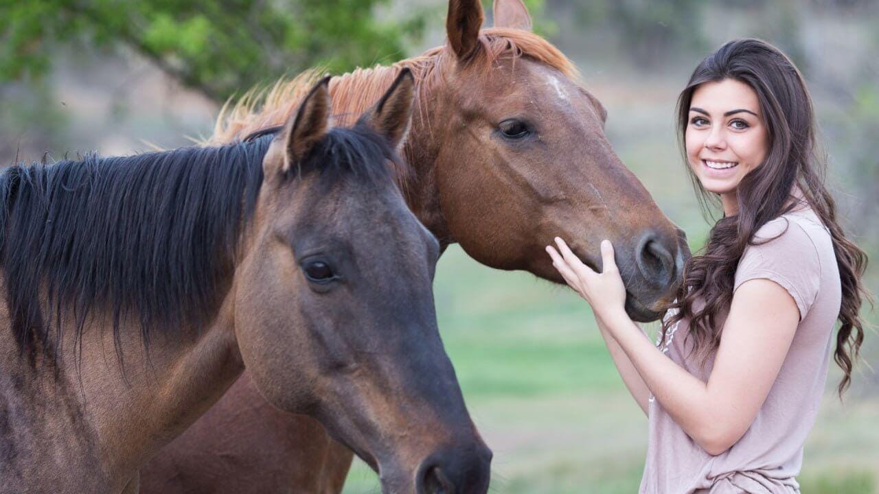 Teen girl smiling while connecting with two horses during a peaceful outdoor session at Spirited Hooves
