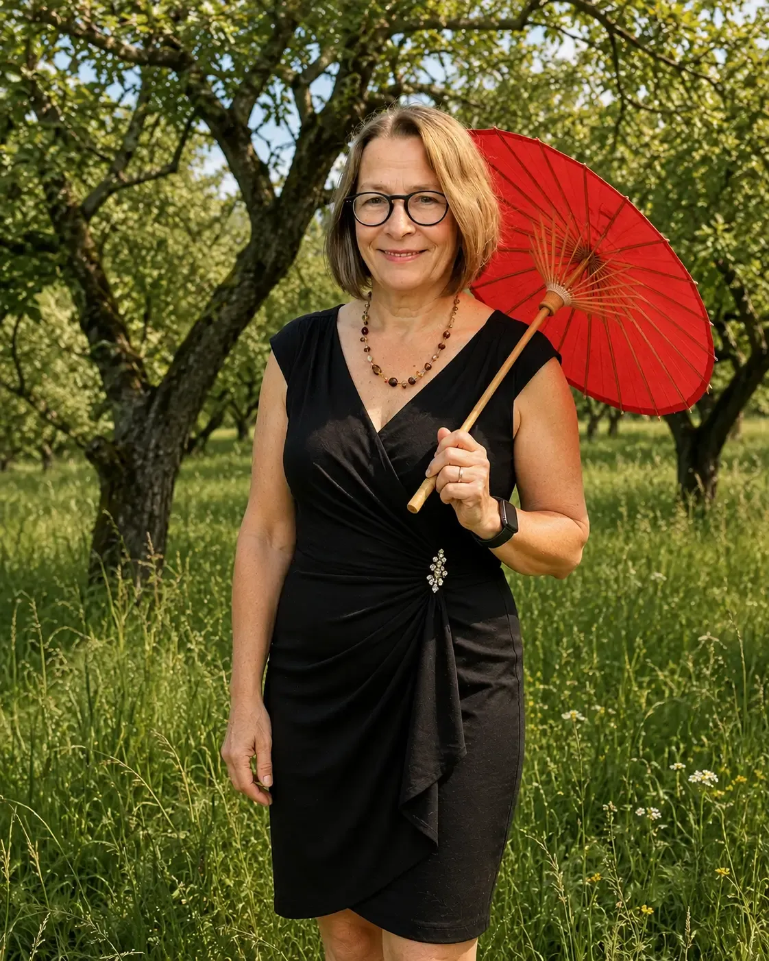 Birgit Baindl mit KI umgestylt in schwarzem Cocktailkleid mit rotem Sonnenschirm, lächelnd in die Kamera, Wiese mit Obstbäumen im Hintergrund