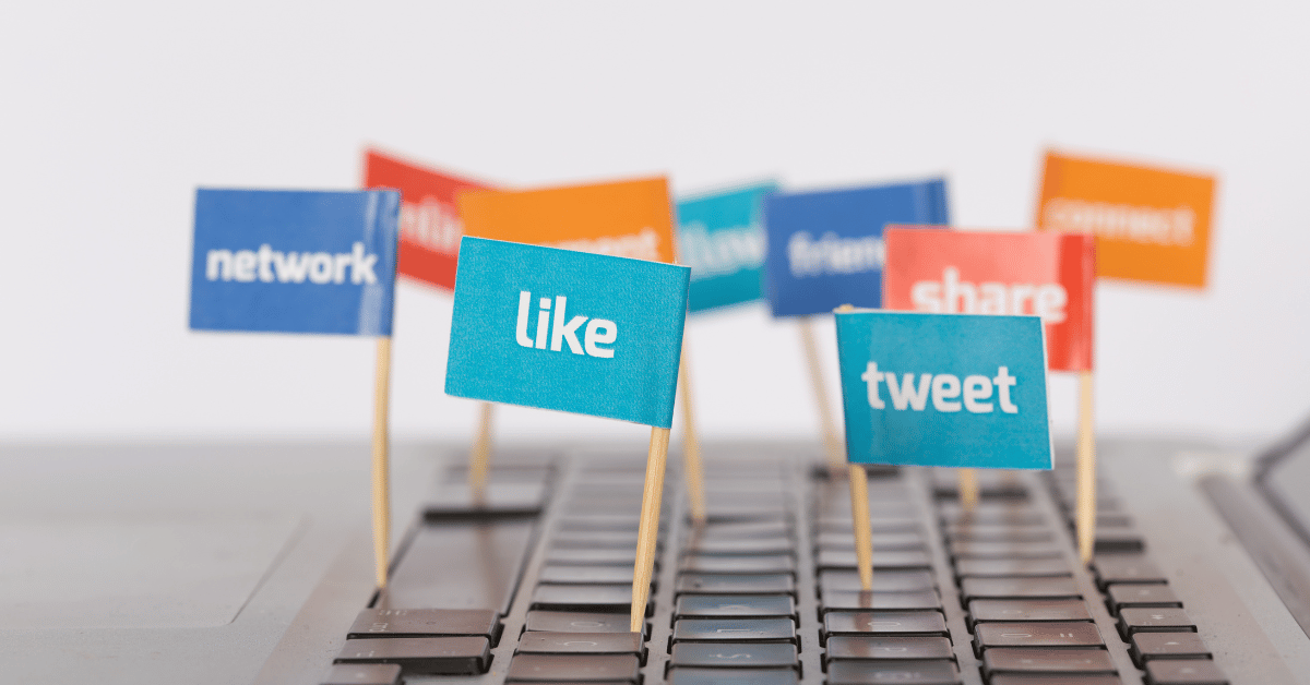 A visual representation of social media engagement, depicting small flags with words like "Like," "Share," "Tweet," and "Network" inserted into the keys of a laptop keyboard.
