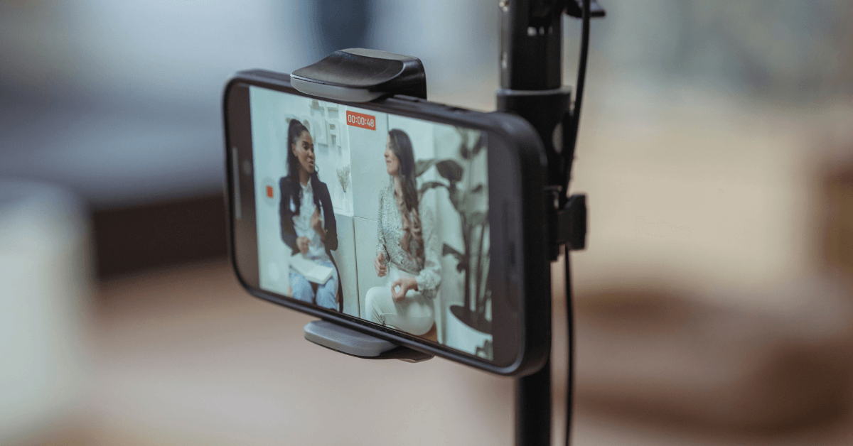 A smartphone mounted on a tripod, capturing professional video content featuring two women discussing a topic.