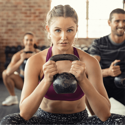 Nainen nostaa kahvakuulaa kuntosalilla.