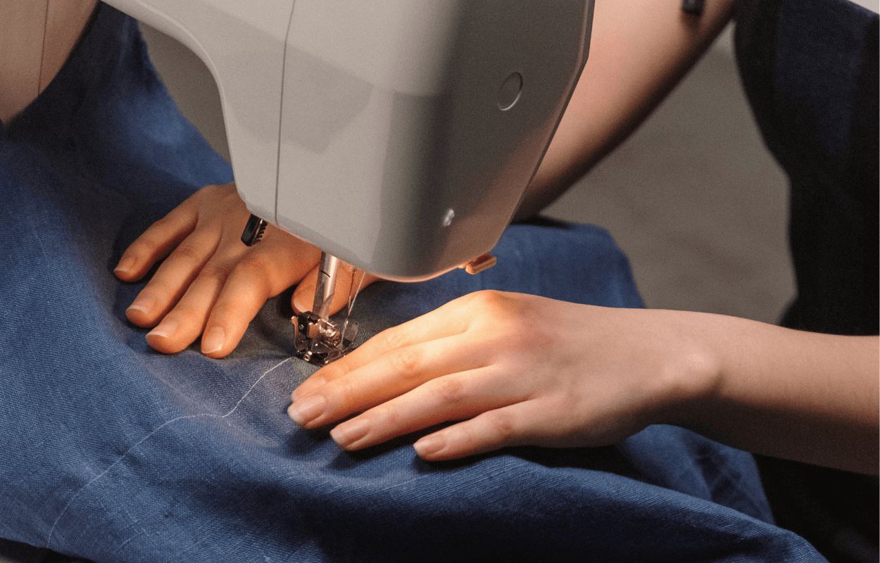 Nahaufnahme von Haenden, die Jeans-Stoff mit einer Naehmaschine naehen