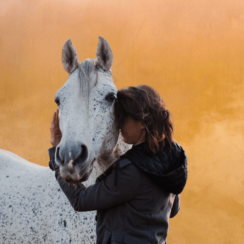 Femme en connexion avec un cheval blanc moucheté, illustrant la relation émotionnelle et transformative en équicoaching