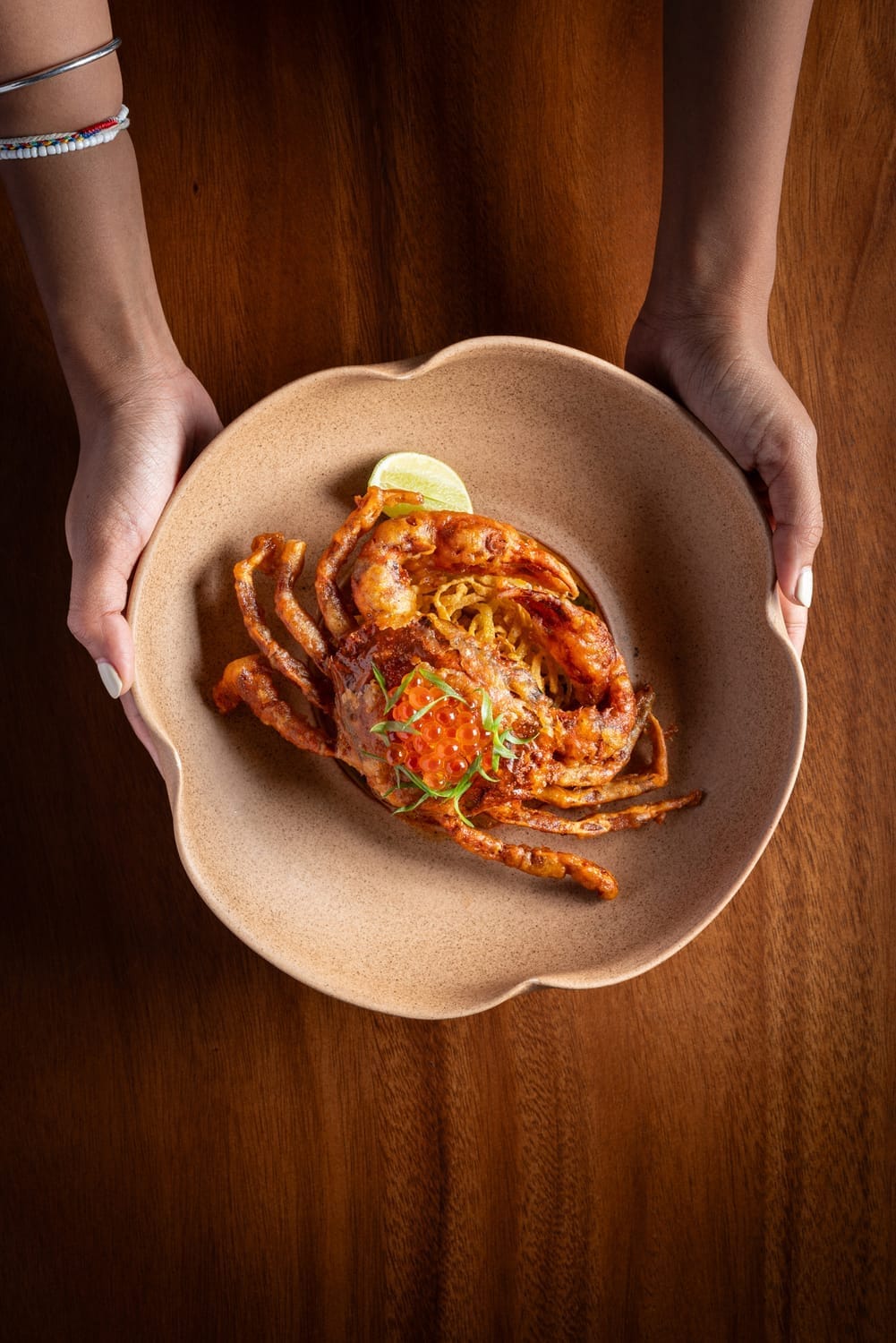 Hands serving a crab dish on warm wood, shot by Diego Arenas