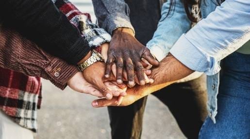 A group of 4 people smiling with their arms all up in the centre putting them together as if they're clapping!