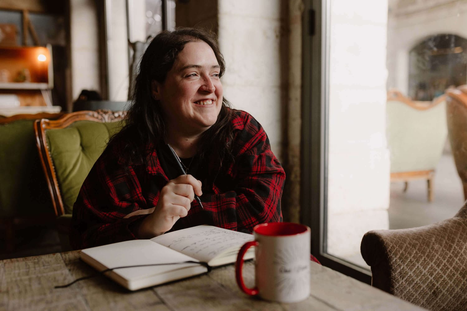Portrait de Noémie Barronie assise à une table, carnet ouvert et tasse posée devant elle.