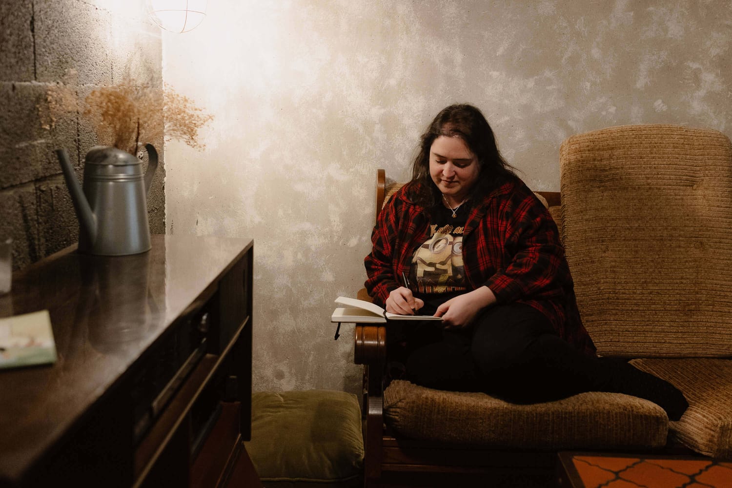 Noémie Barronie assise dans un fauteuil, en train d’écrire dans un carnet.