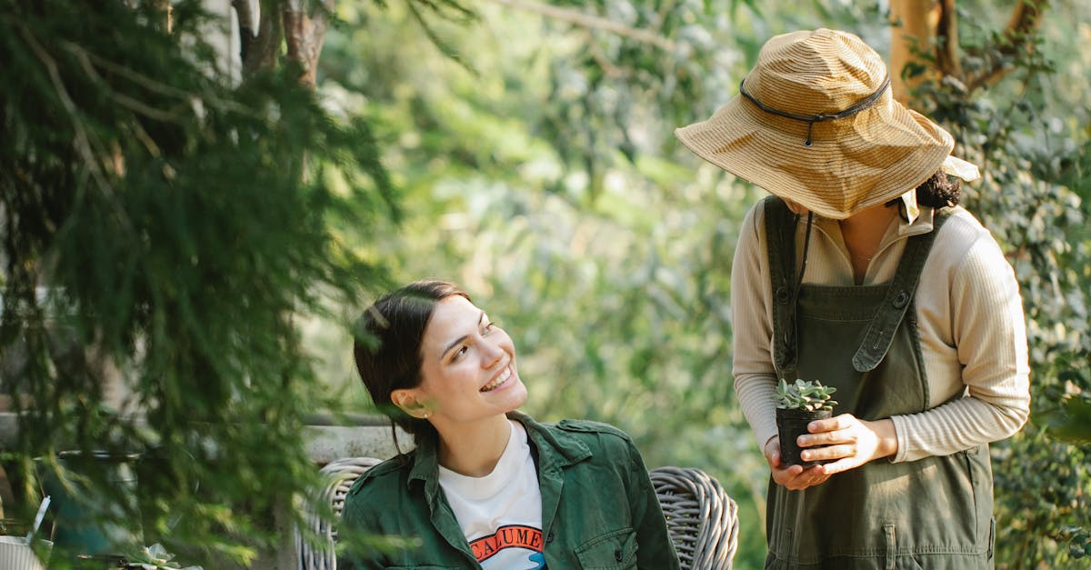 Cheerful ethnic female gardeners with book and beverage chatting in botanical garden