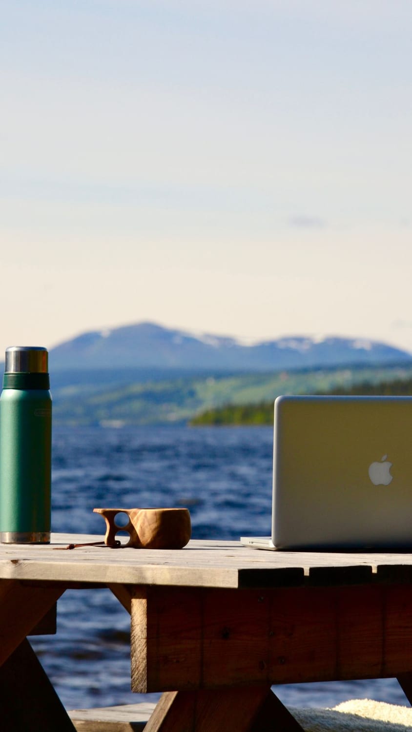 The LakeHouse Media lake office, a MacBook, a thermos and a wooden coffee cup with a lake view