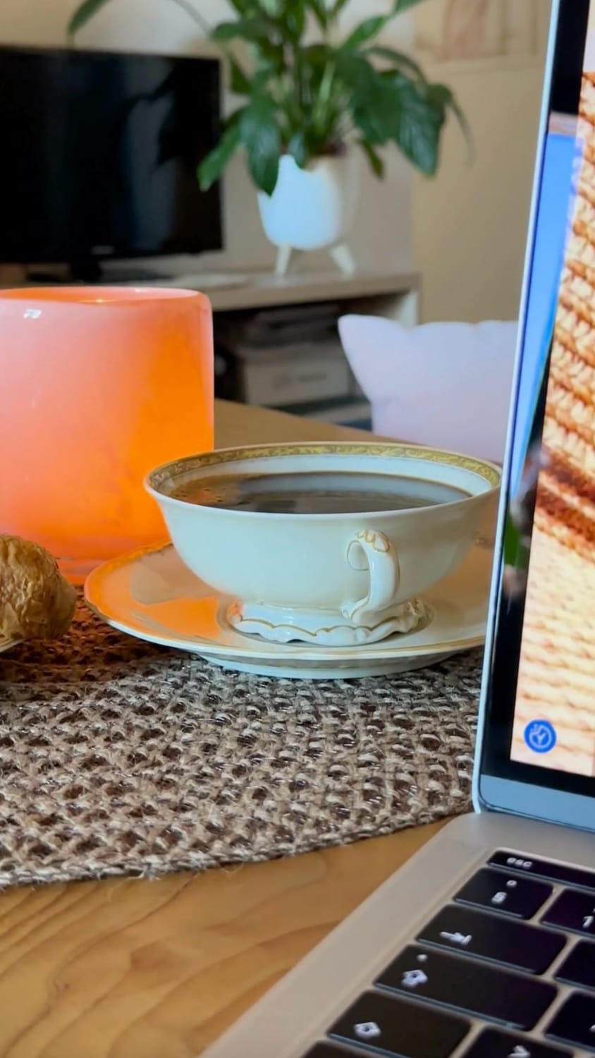 An antique porcelain cup on a wooden table in Florence, part of a cozy morning routine for a laptop-based Handbag Office.