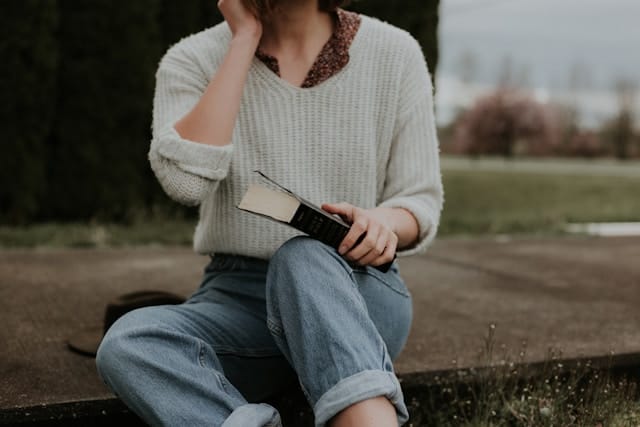Woman in white sweater and jeans with book