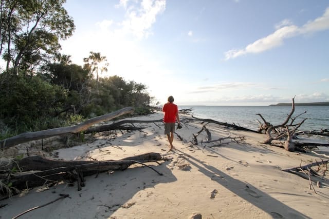 Man in red shirt, shoes in hand walking on the beach