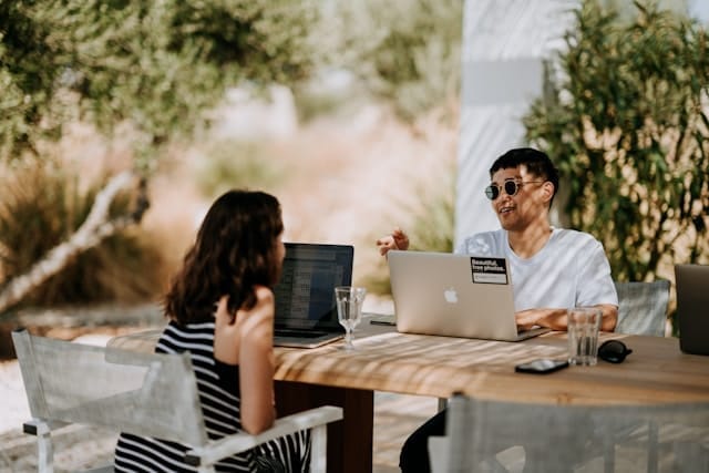 Man and woman outside with laptops.