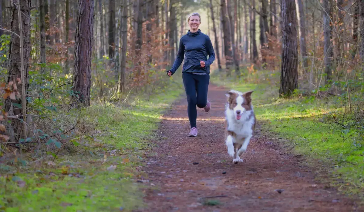 Woman jogging outdoors with her dog to support gut health through exercise and stress relief.