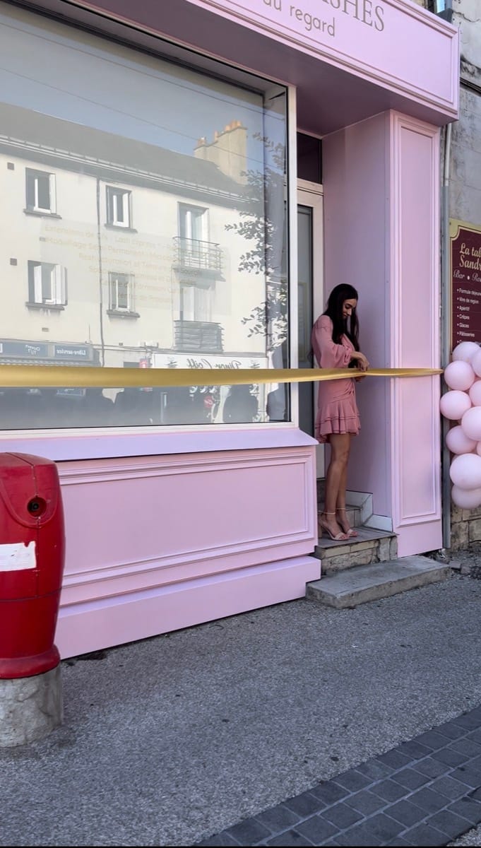 Joanna coupe le ruban devant la façade rose du premier institut