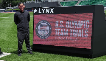 Coach Diego Vela junto a un cartel de competencia NCAA