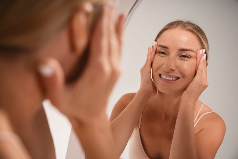 Femme souriante appliquant un soin sur son visage devant un miroir