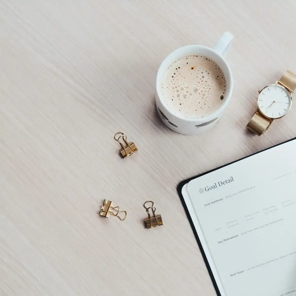 A clean workspace with a "Goal Detail" planner, coffee, and a watch, symbolizing careful planning for effective business growth strategies.