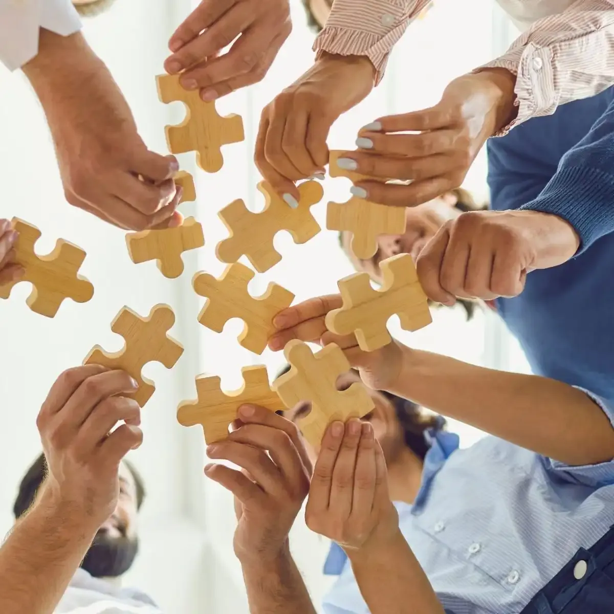 Low-angle shot of a diverse team holding wooden puzzle pieces together in a circle, symbolizing the collaboration needed for successful business growth strategies.