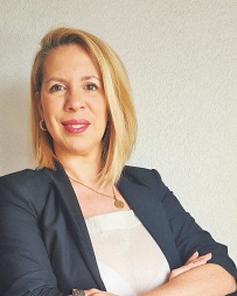 Ani seria, de brazos cruzados con blazer negro, en pose de foto profesional