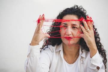 Marianella Ruiz con hilo rojo enredado entre las manos delante del rostro