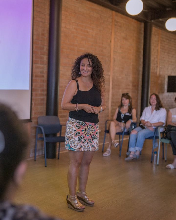 Marianella Ruiz sonriendo en un taller, con mujeres sentadas detrás