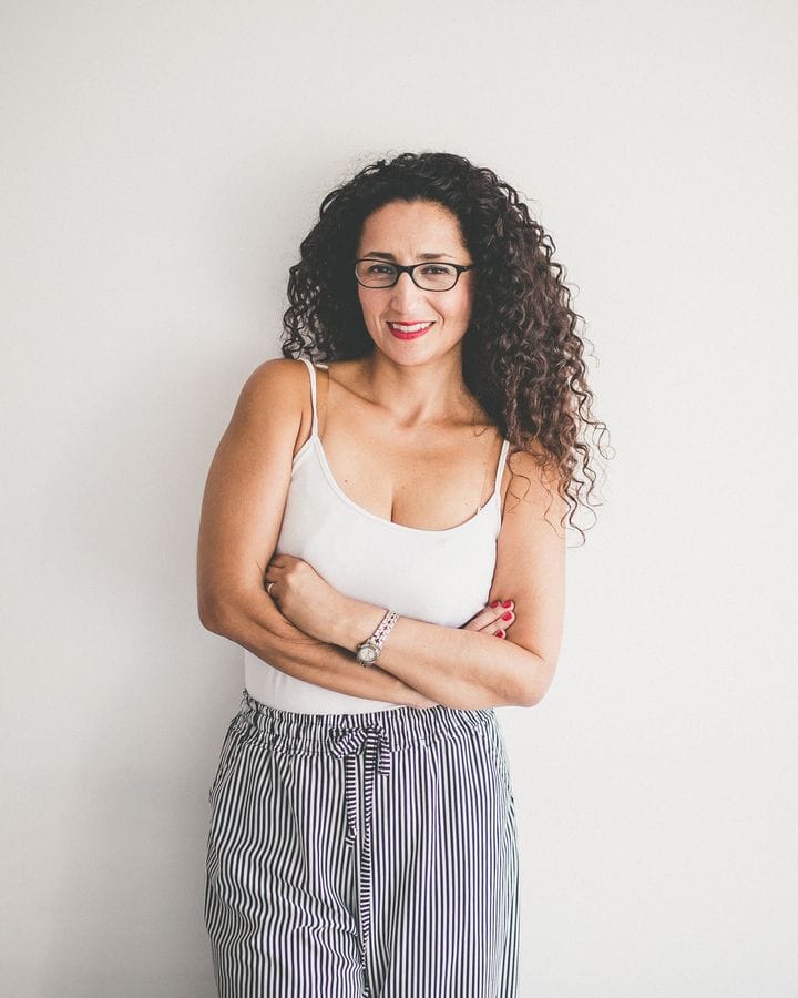 Marianella Ruiz con lentes y polera blanca, sonriendo con los brazos cruzados