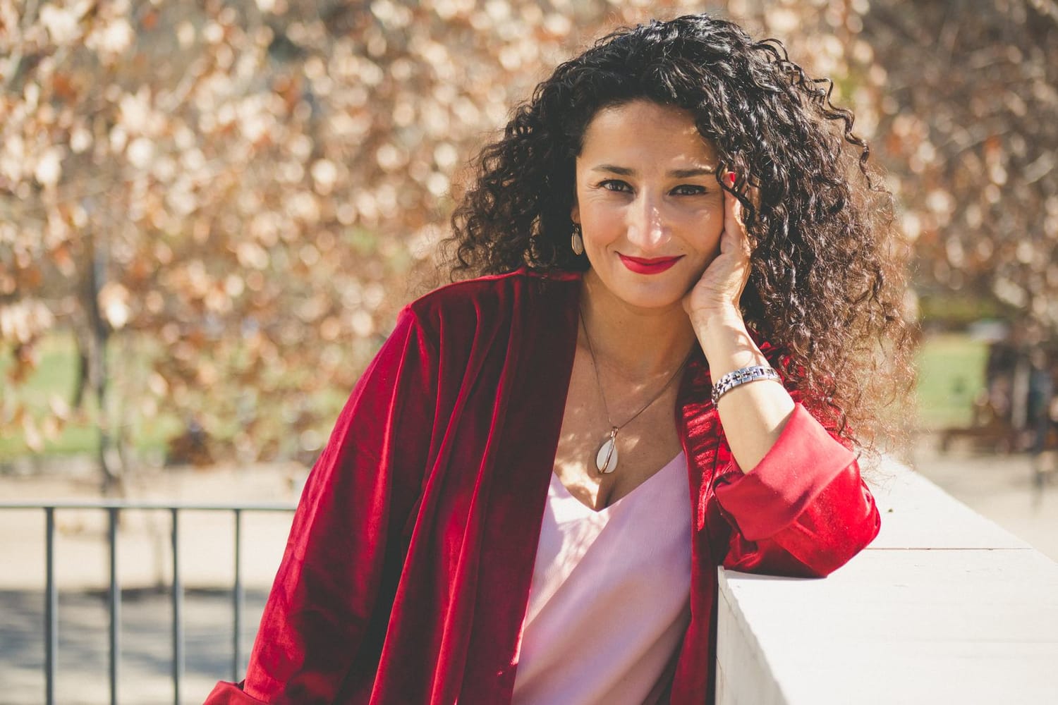 Marianella Ruiz sonriendo, con una chaqueta roja y la mano en la mejilla