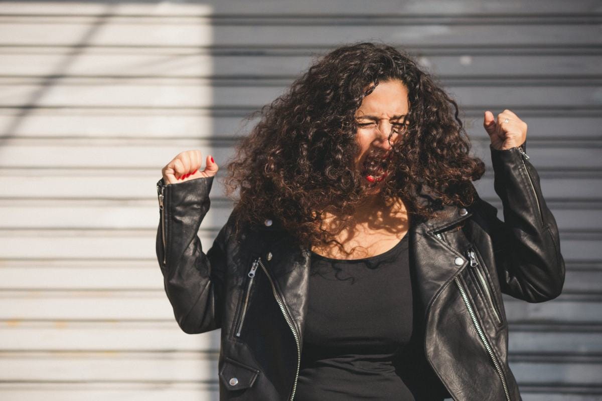 Marianella Ruiz con chaqueta negra de cuero, con los puños arriba y el pelo al viento, gritando con fuerza