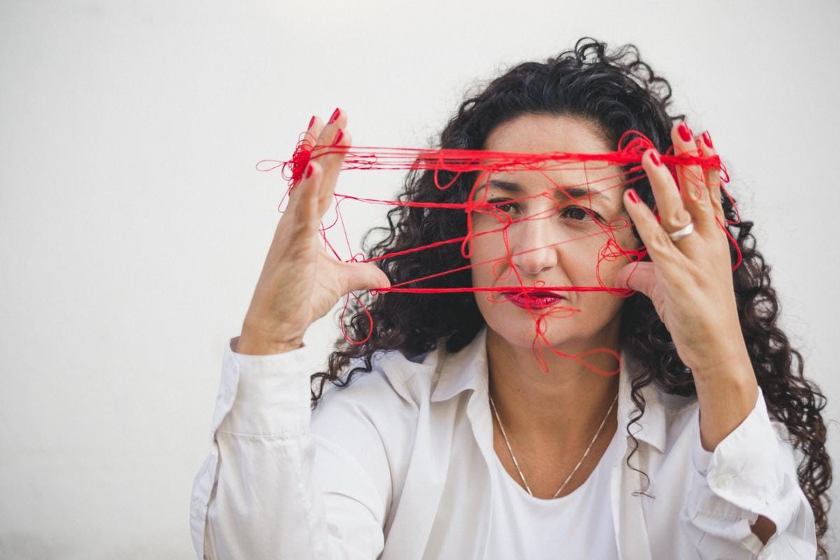 Marianella Ruiz con hilo rojo enredado entre las manos delante del rostro