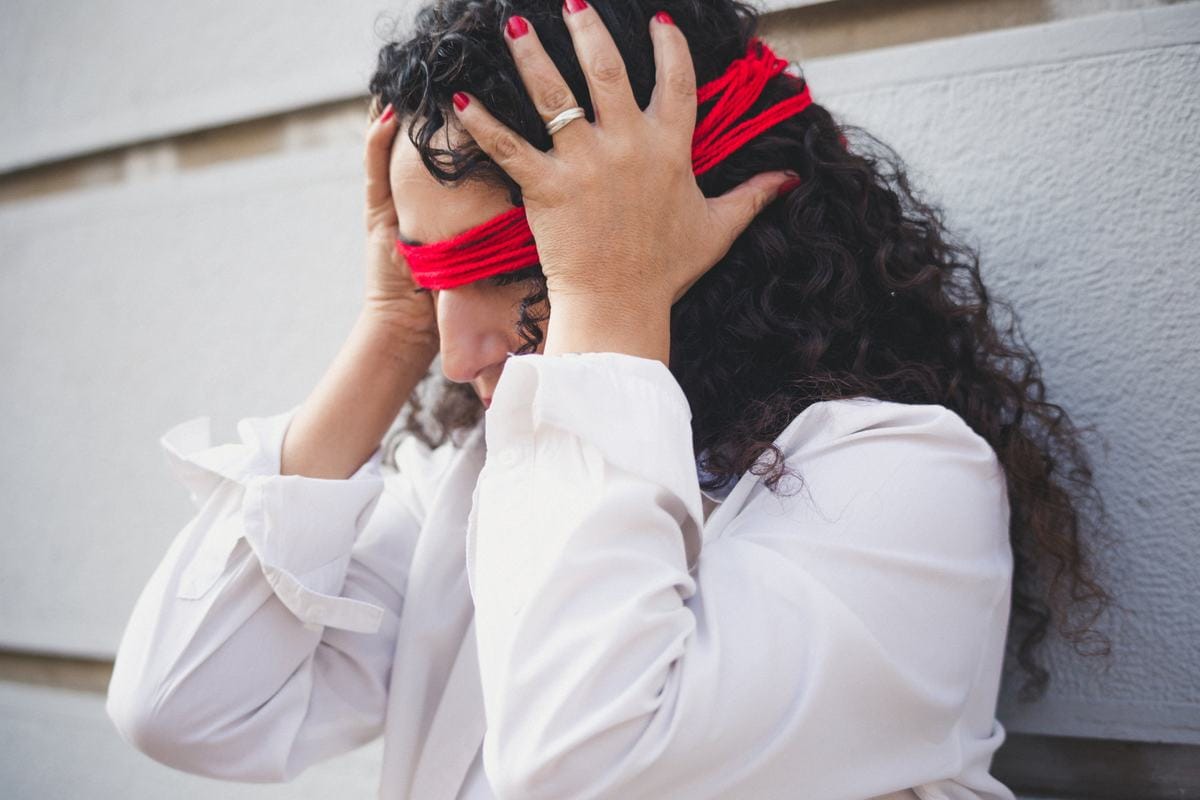 Marianella Ruiz con camisa blanca y un hilo rojo en la frente, con las manos en la cabeza