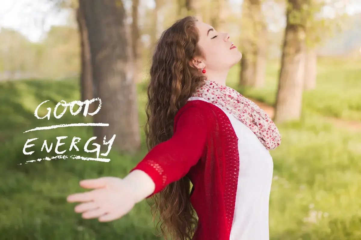 A vibrant woman over 50 stretching her arms wide in nature, representing good energy, vitality, and emotional well-being.