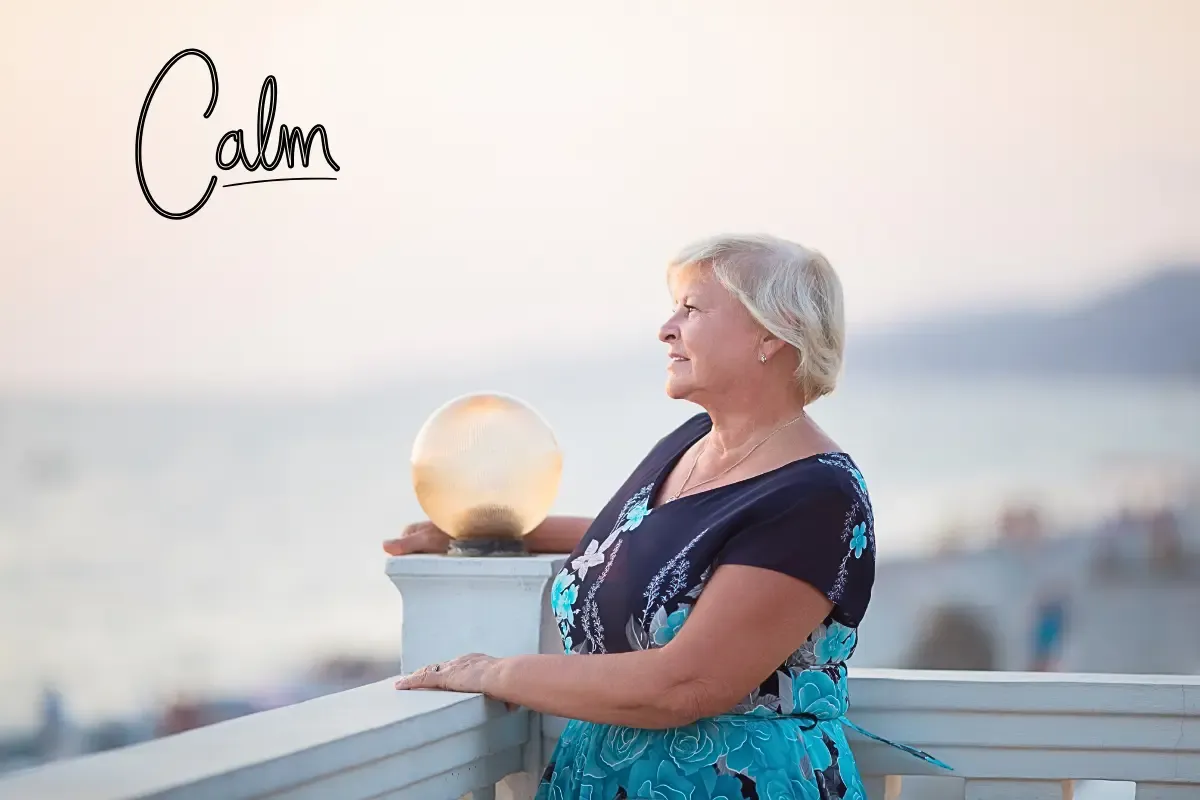 A calm woman over 50 looking out at the sea during sunset, learning how to wind down and release daily stress.