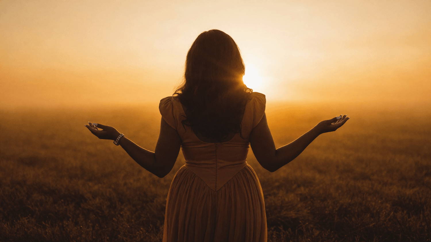 Woman standing in golden hour field with arms open, representing the moment of returning to God after a faith crisis and spiritual dry season