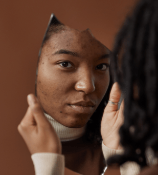 A woman  looking into a mirror with a soft, peaceful expression. Emotion: Reflection, purpose, identity