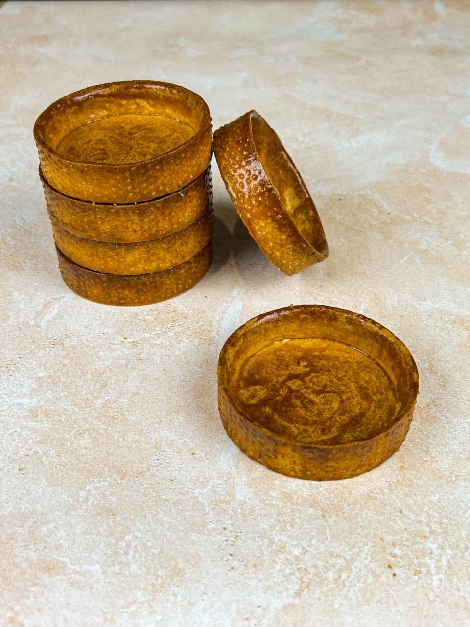 Fonds de tartelettes en pâte sucrée bien dorés, empilés sur un plan de travail