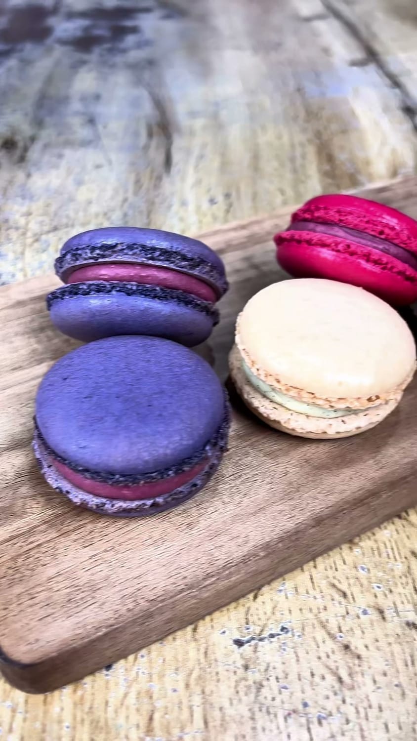 Macarons maison violets, roses et beiges, posés sur une planche en bois