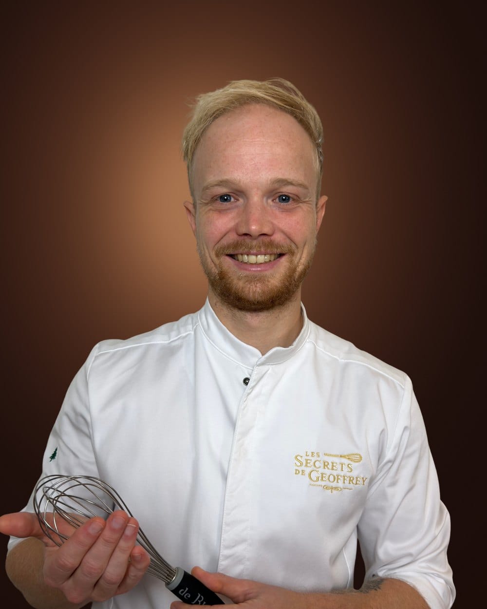 Geoffrey en veste de pâtissier, un fouet à la main