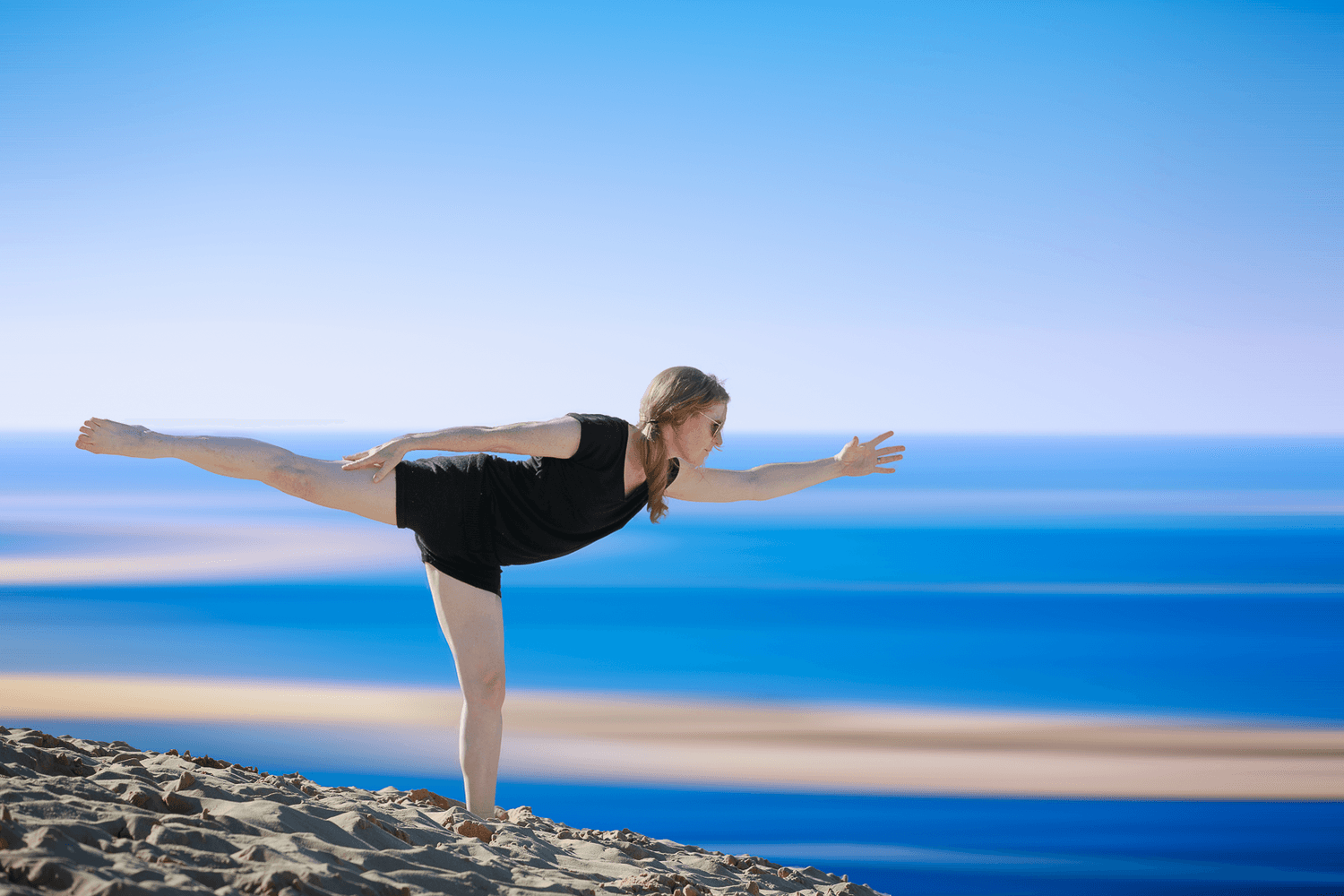 Femme en posture de yoga sur la dune, face à l'océan, au coucher du soleil