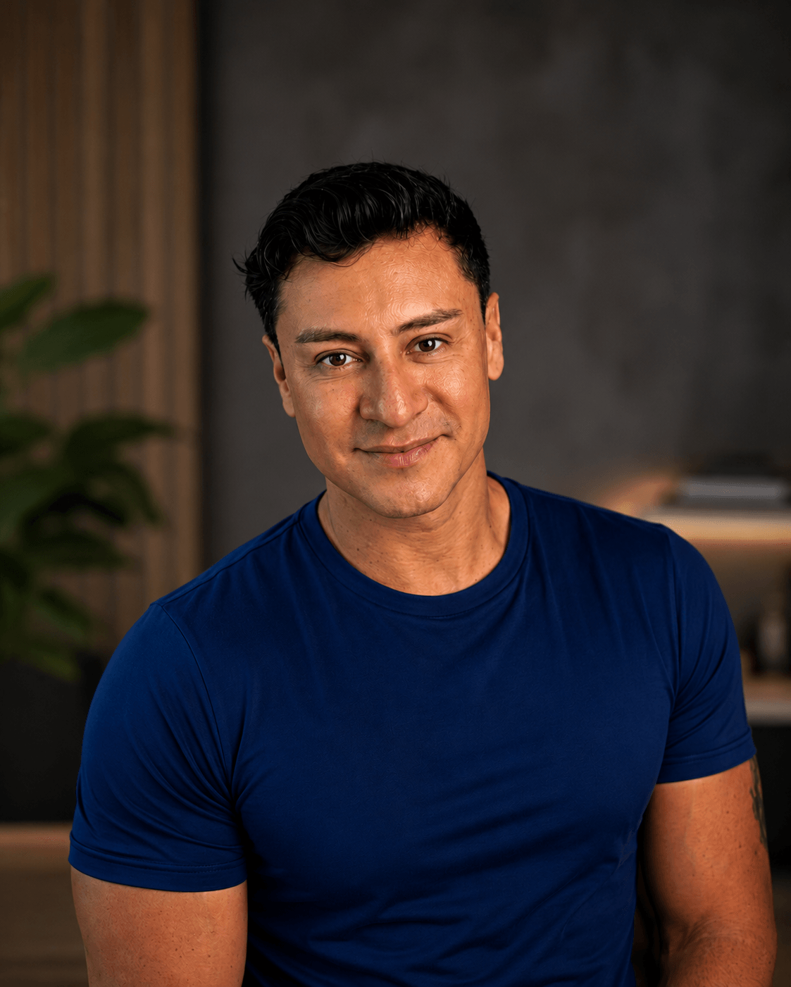 Retrato profesional de Alex García, mentor de autoconocimiento, desarrollo personal y gestión emocional. Aparece con camiseta azul marino y una expresión cercana y segura, mirando directamente a cámara. El fondo moderno y elegante, con iluminación cálida y desenfocada, transmite confianza, calma y profesionalismo.