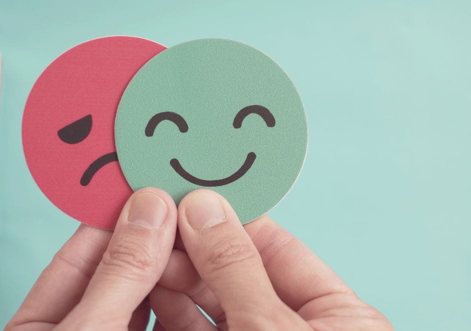 Une main tient deux visages en papier, un triste et un souriant, pour illustrer la différence entre deux modèles d'affiliation