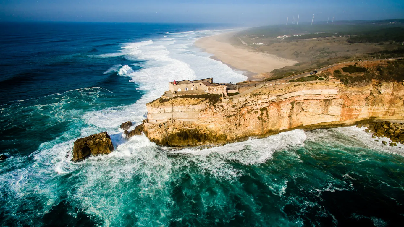Praia de Nazaré, com o farol e as ondas gigantes ao fundo.