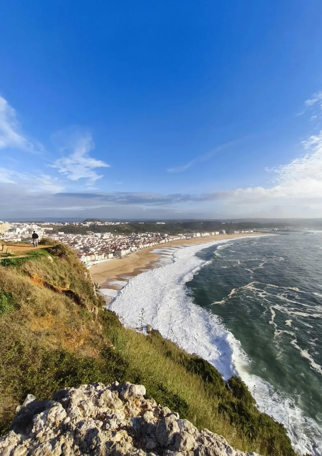 esta imagem mostra uma vista onde se consegue ver a cidade e a braia e o mar em Nazaré.
