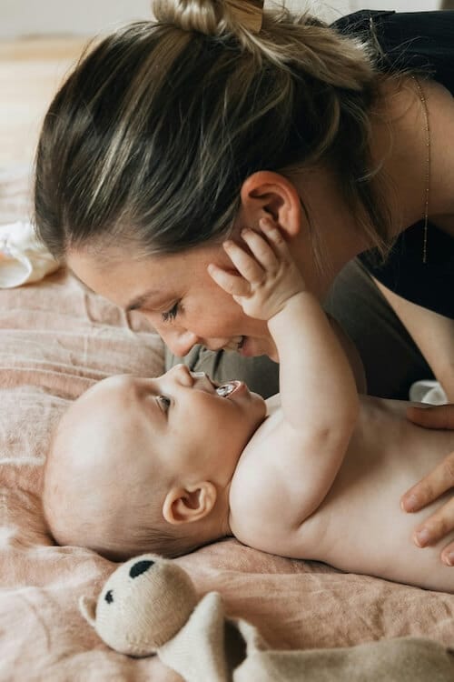 Un bébé sur le dos qui joue avec le visage de sa maman