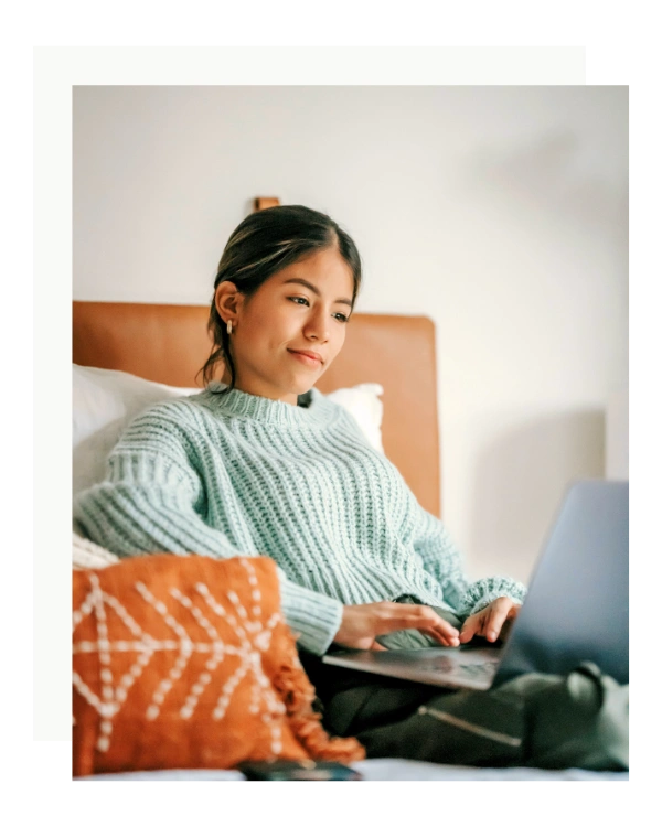 woman wearing a blue pullover happily typing on her laptop