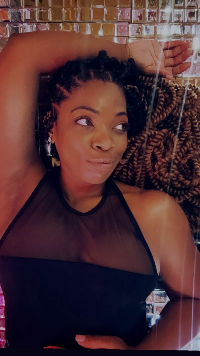 Kala C. Simmons, MSW | Confidence & Authenticity Coach, Visionary Founder & CEO of The Kollective lying down on a mirrored back grouned with a mischievous smirk on her face