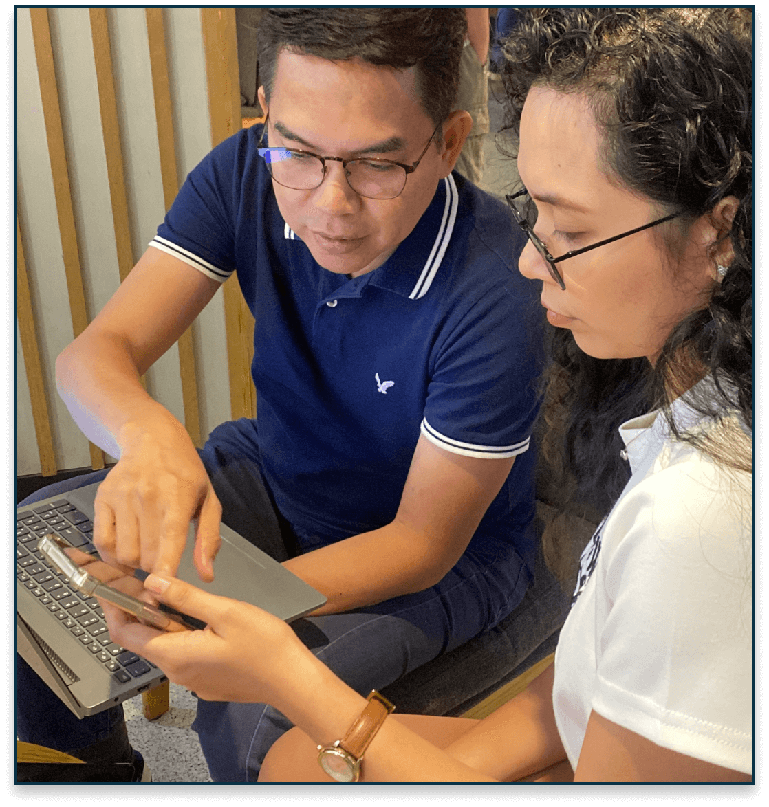Advisor guiding a client, pointing to a phone screen beside a laptop during consultation.