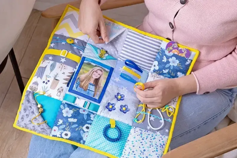 Large fidget blanket for dementia patients with multiple textures, zippers, and buttons designed to reduce anxiety and keep hands busy.